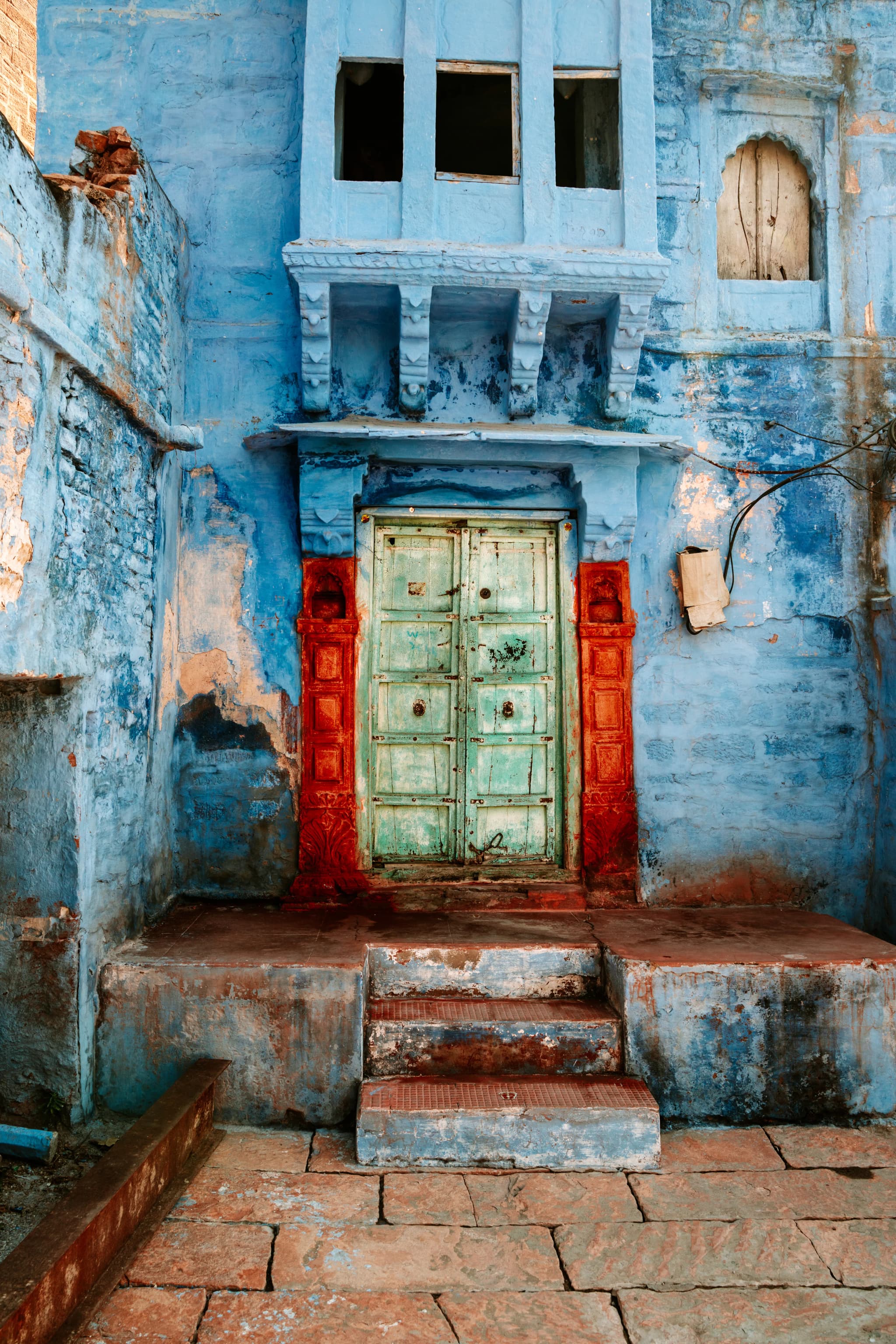 Blue-washed house front with a green wooden door in a red frame above worn stone steps