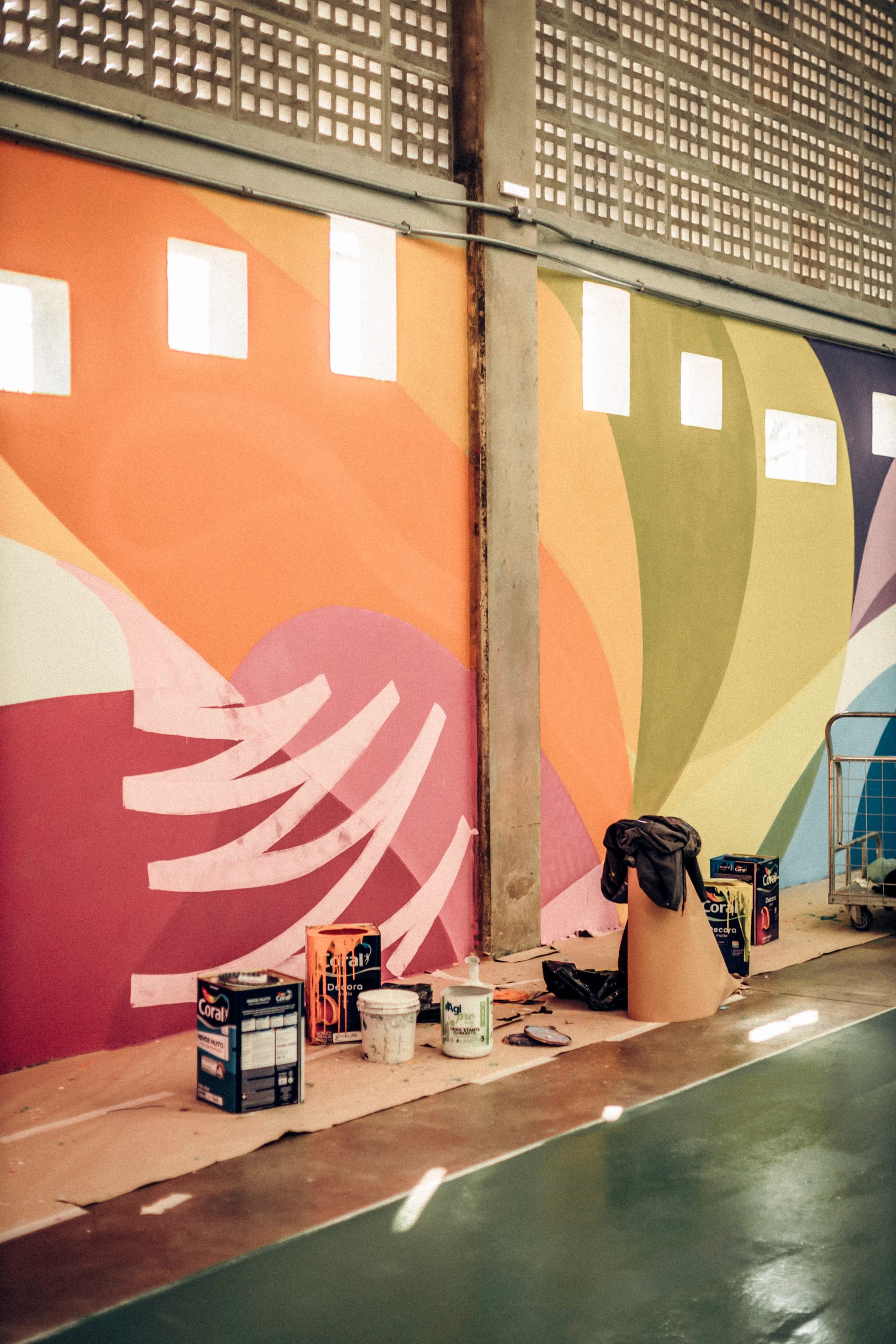 Paint buckets on floor paper beside a large, colourful painted mural wall