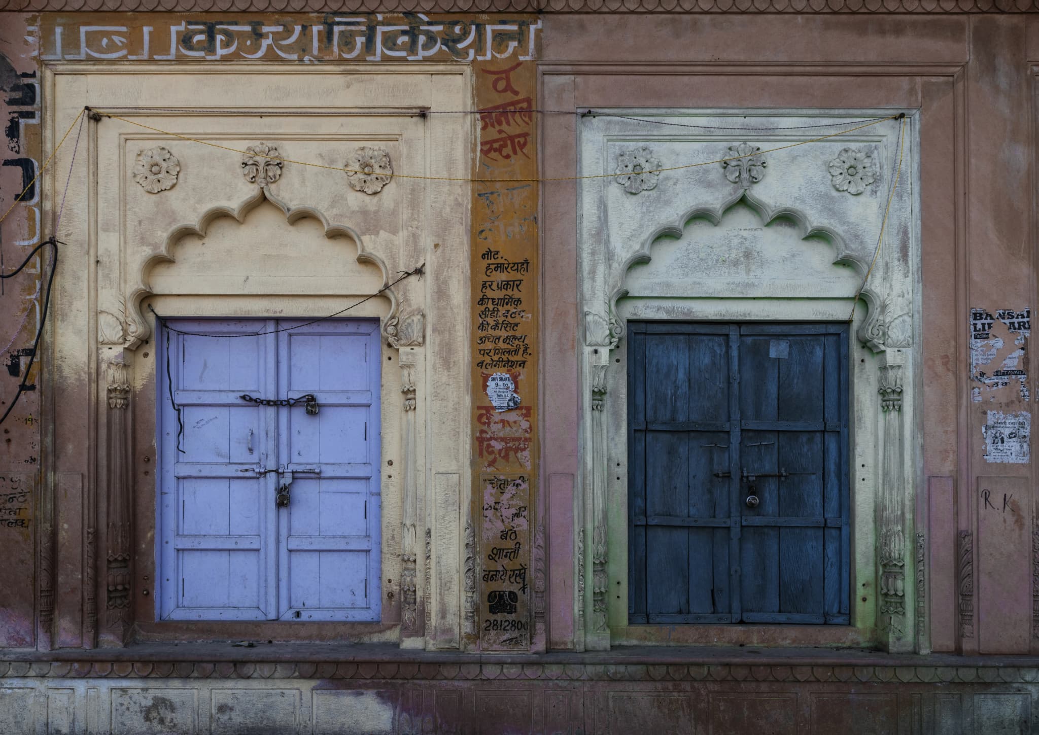 Two old doors painted lavender and deep blue in carved cream archways on a weathered wall