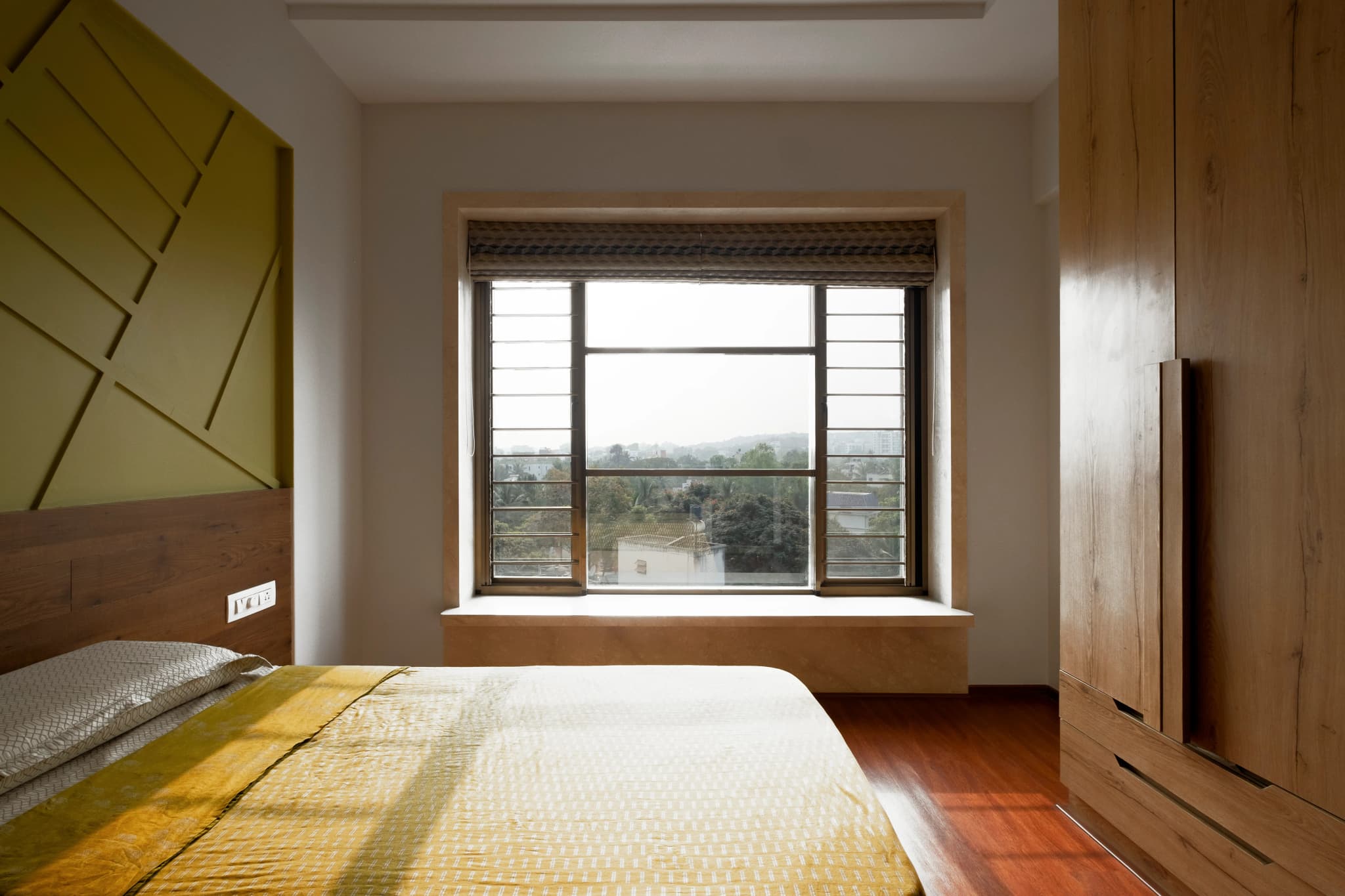 Bright bedroom with plain walls, a wooden wardrobe and a large window