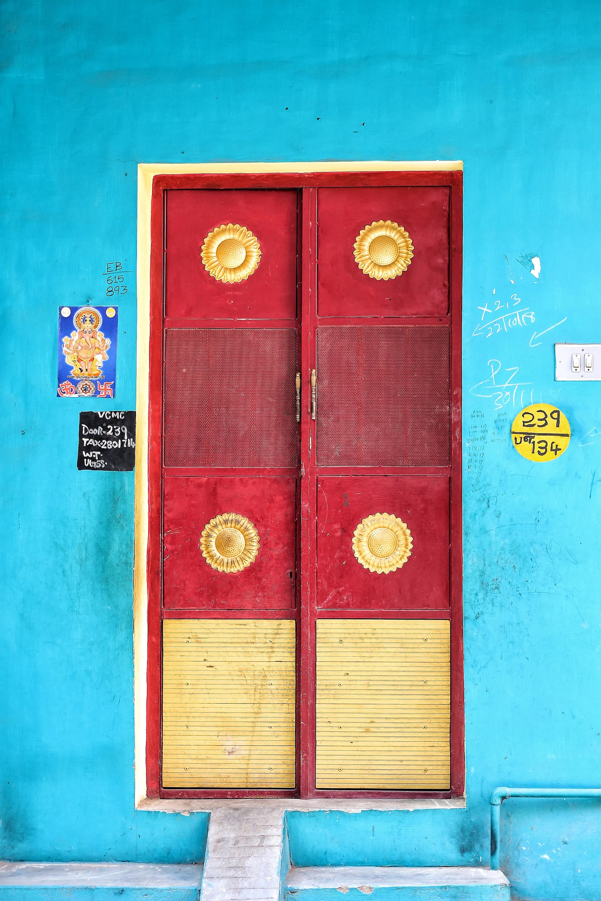 Red and yellow double door with brass medallions set in a bright turquoise wall