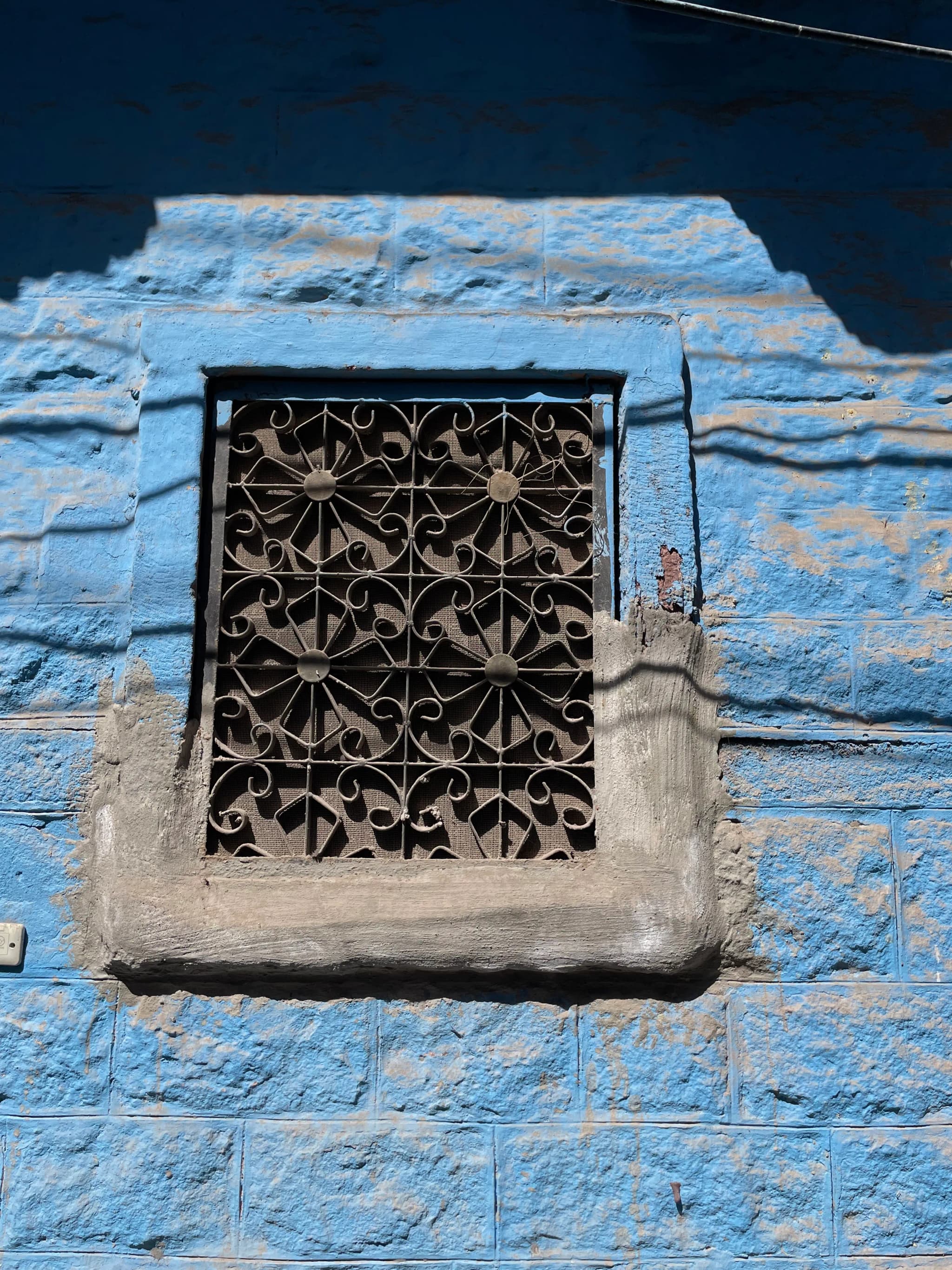 Ornate black iron window grill set in a textured sky-blue wall