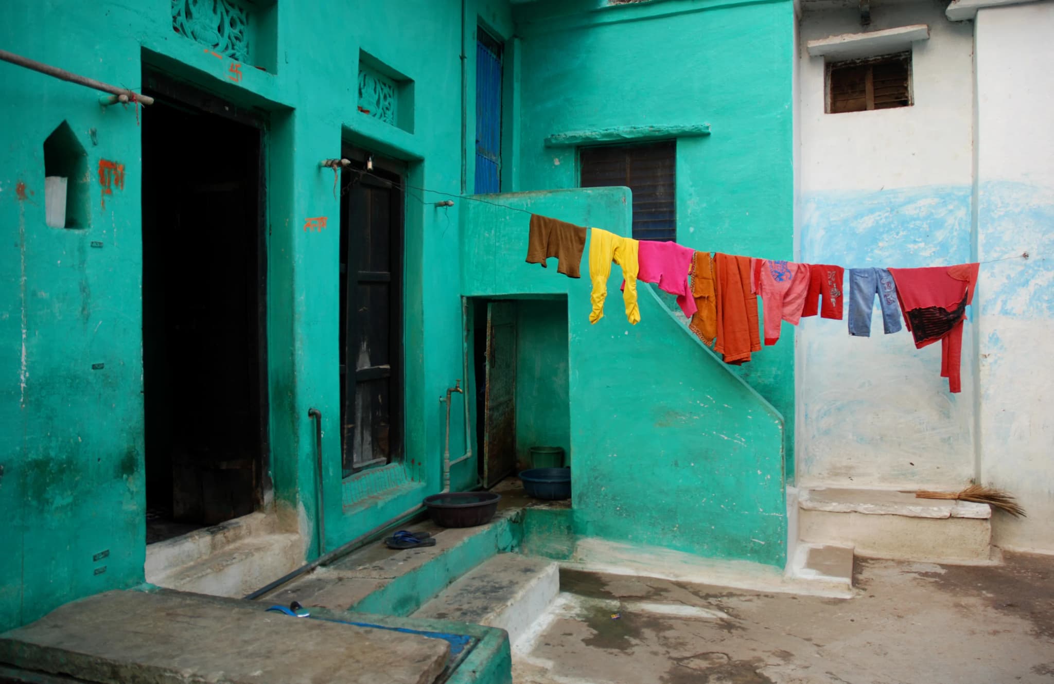 Turquoise house with an outdoor staircase and clothes drying on a line across its courtyard