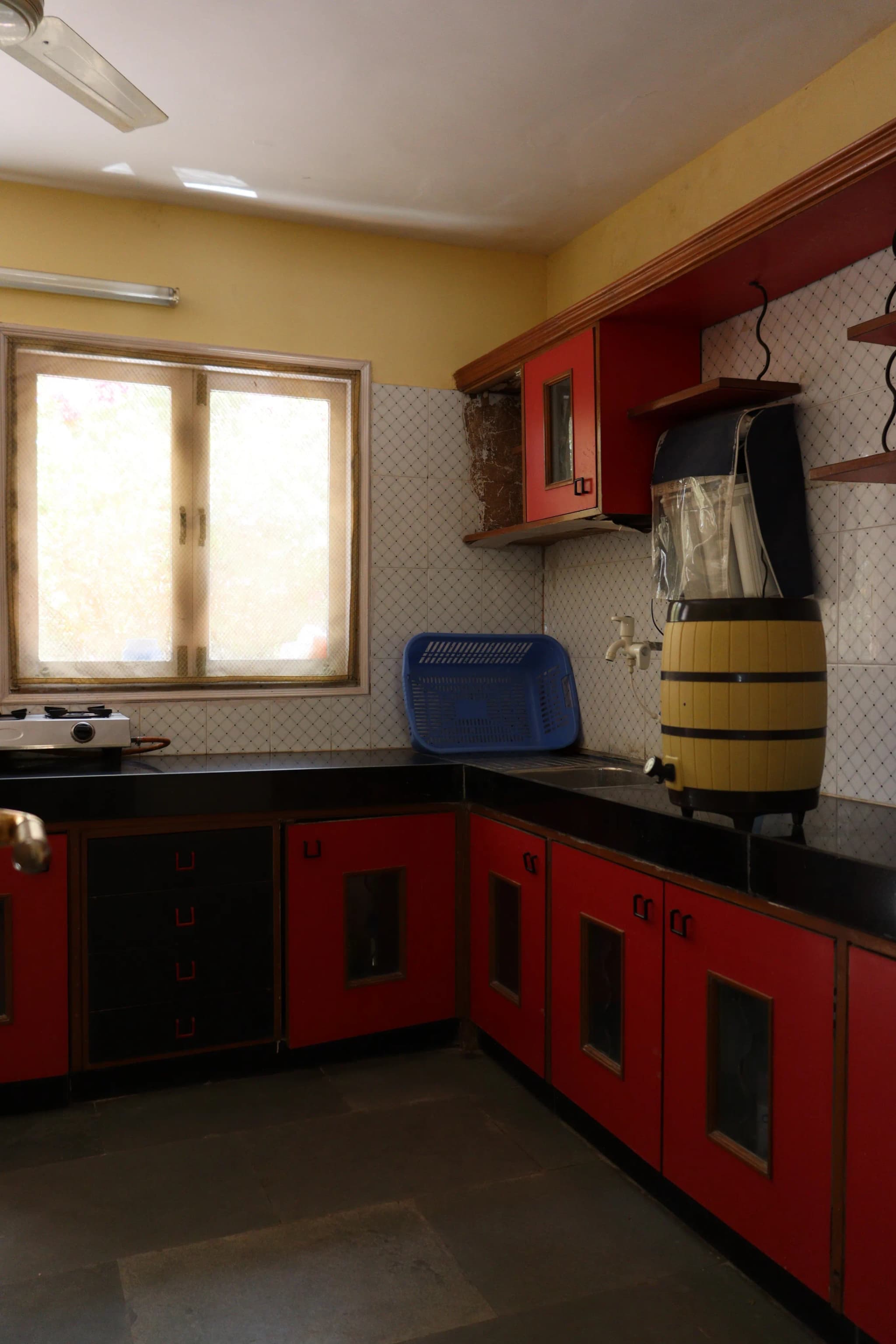 Kitchen with red cabinets, a black counter, white tiles and a window above the stove