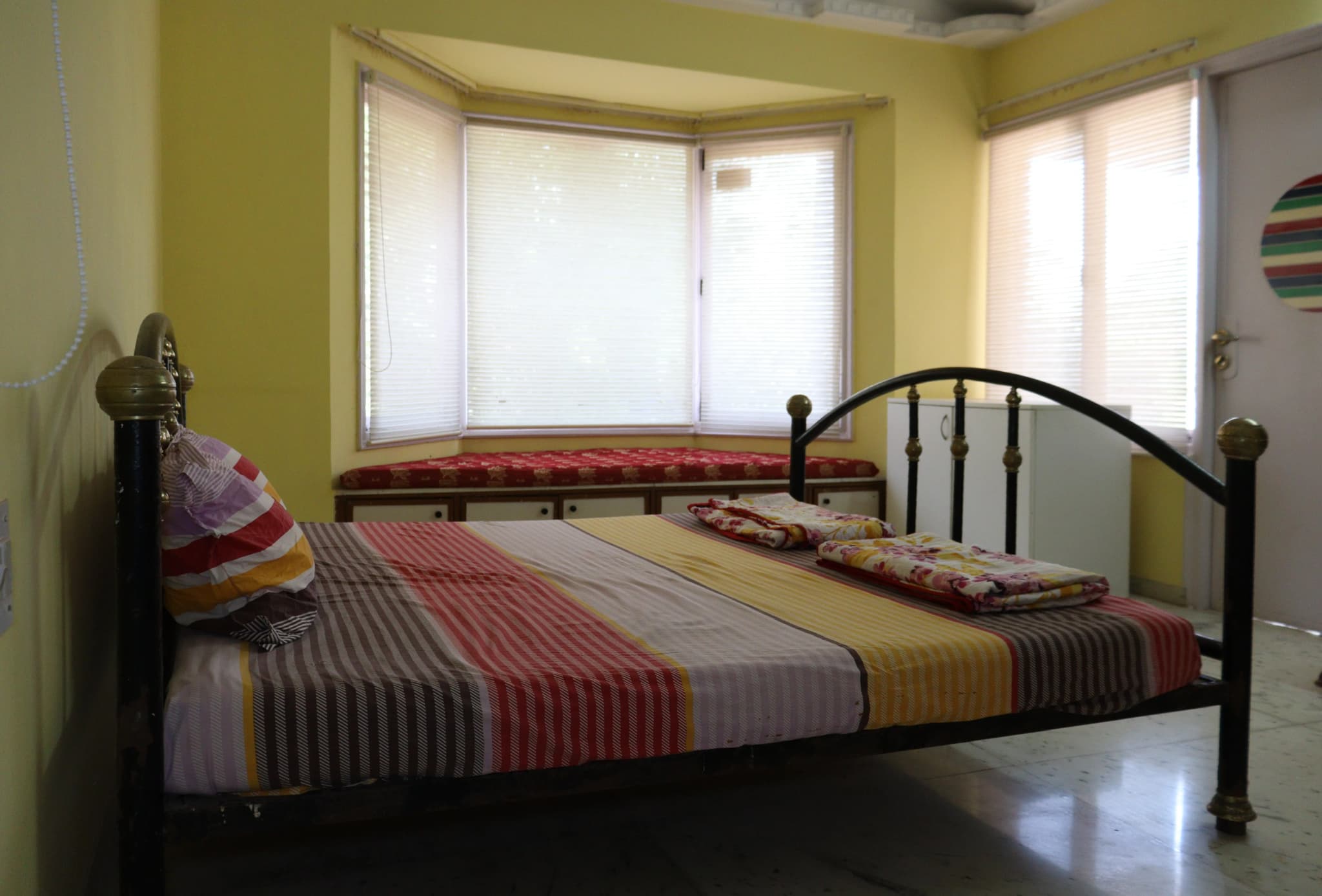 Bedroom with lime-green walls, a bay window and a striped bedspread on an iron bed