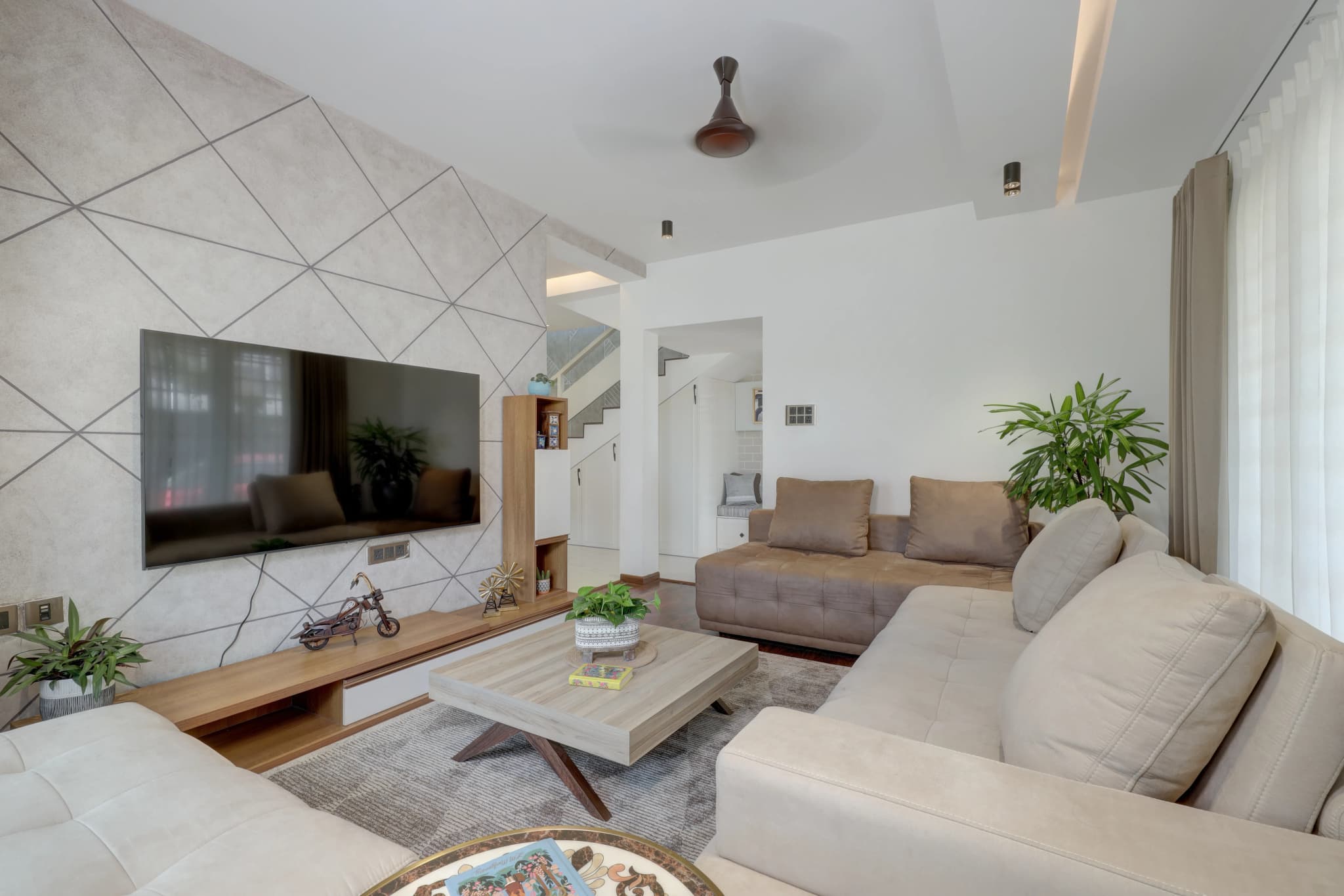Open living room with white walls, a geometric pattern on the TV wall and beige sofas