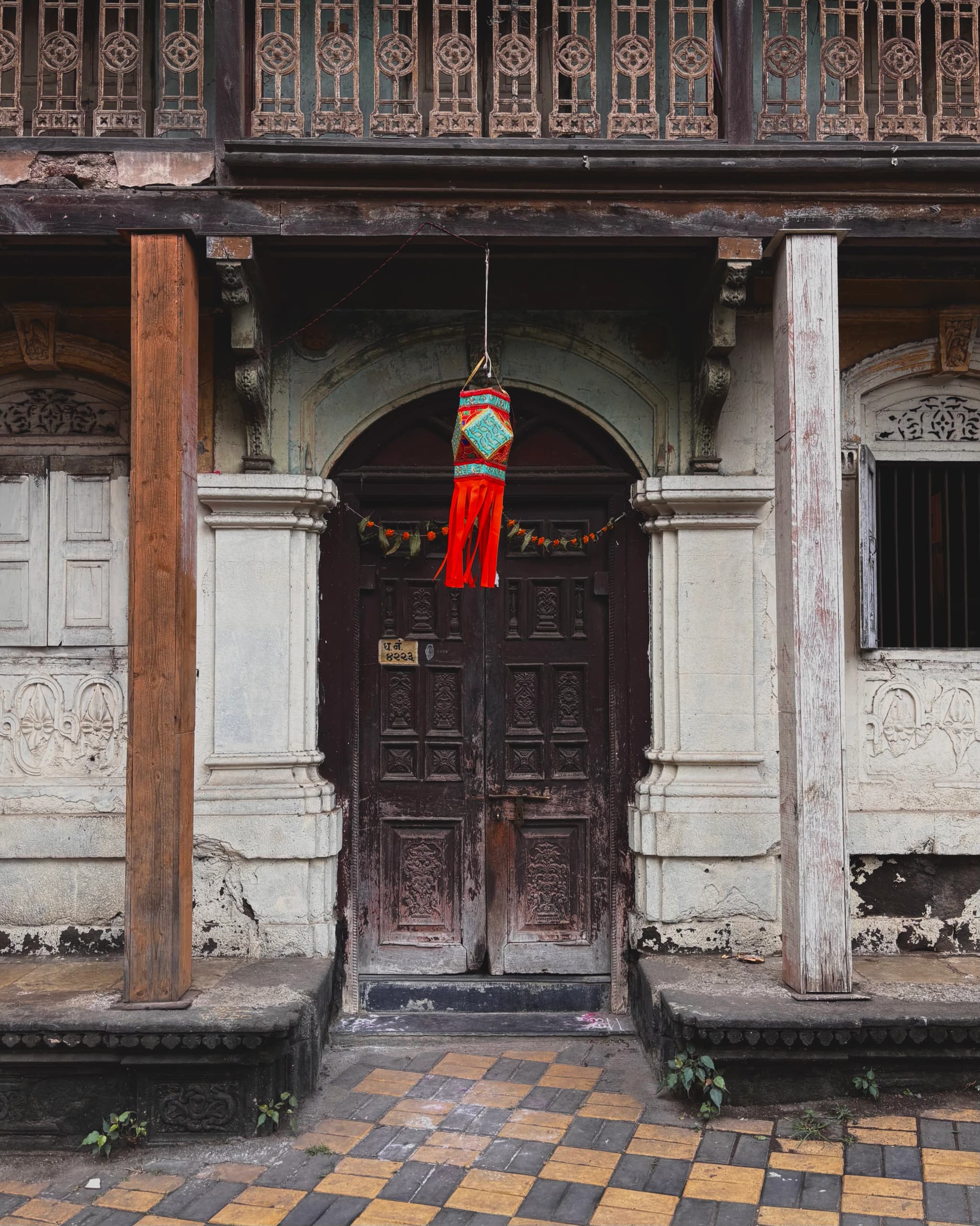 Old house entrance with carved wooden doors, stone pillars and a chequered tiled floor
