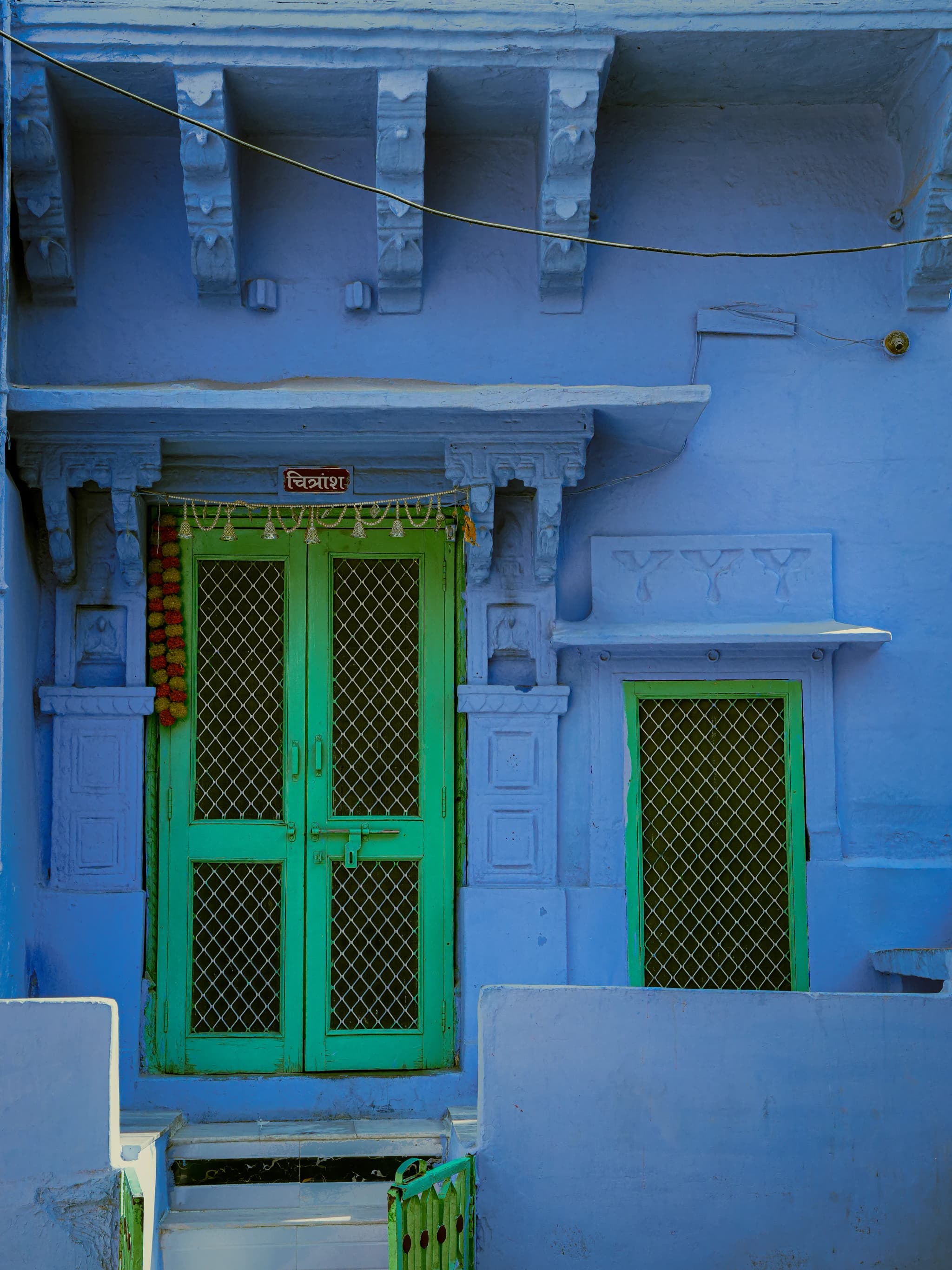 Blue house front with green wooden doors and a green window grill