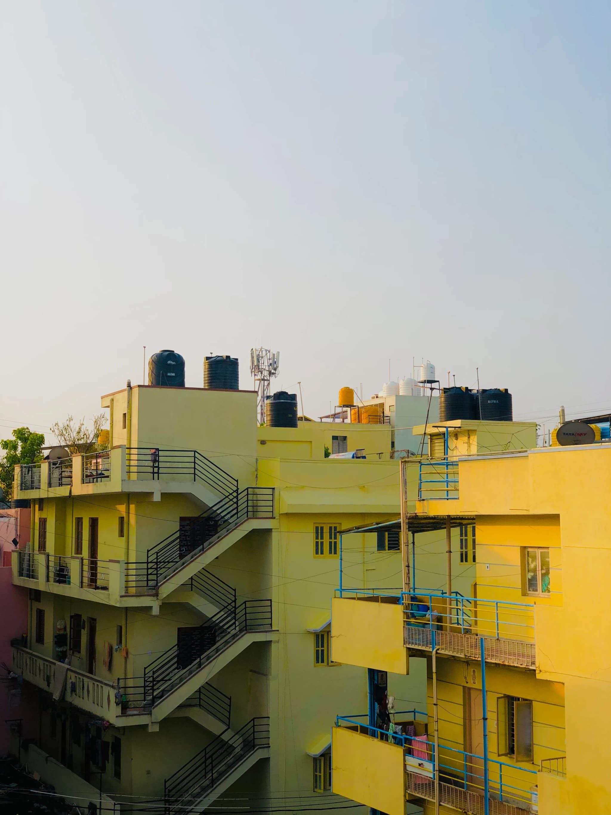 Yellow apartment blocks with green staircases and balconies under a clear sky