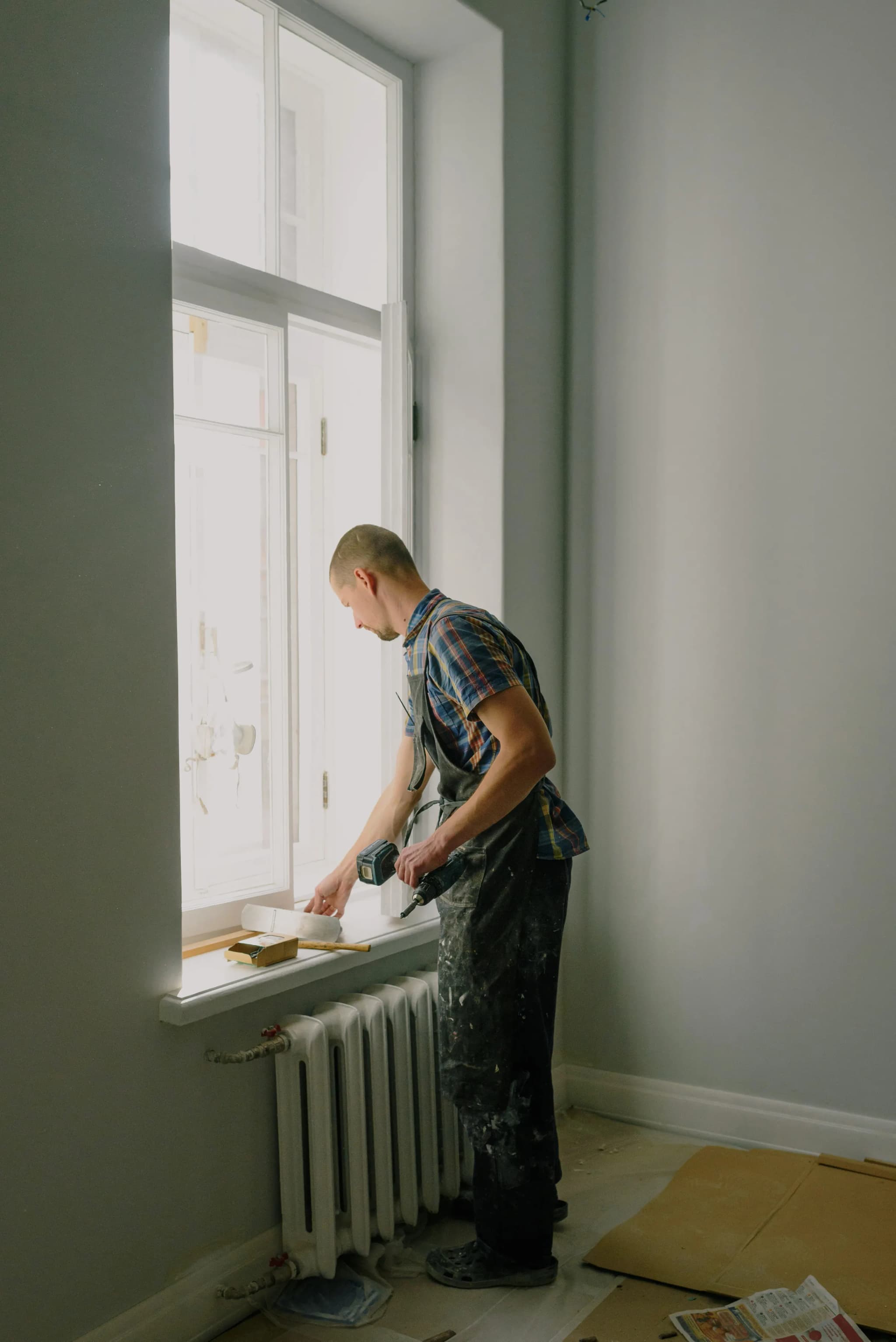 Painter preparing a window sill for painting in a room with pale grey walls