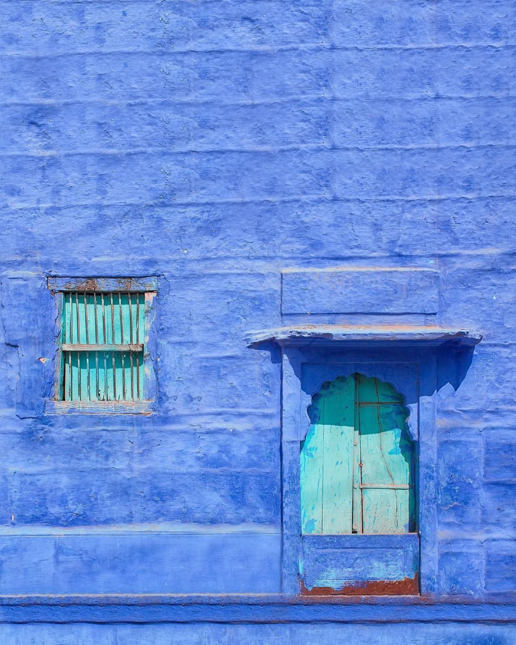 Bright blue wall with two small windows painted turquoise